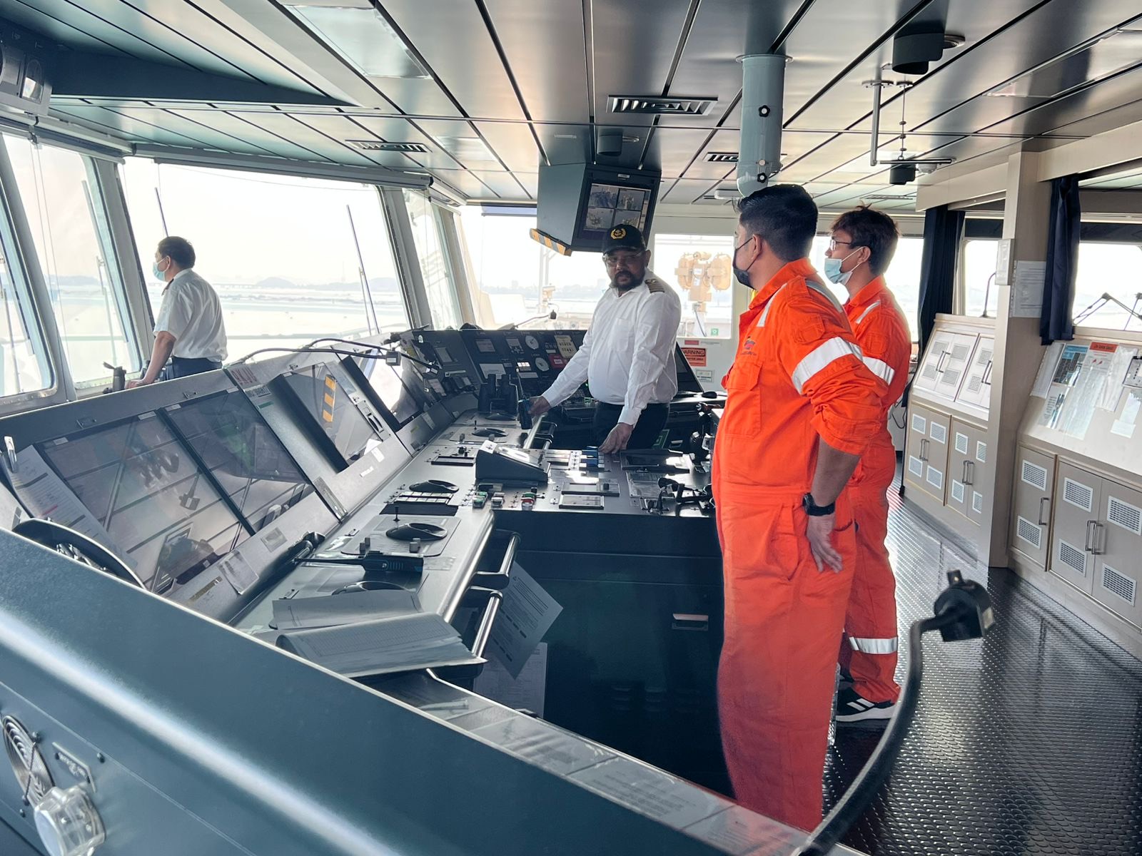 A captain instructs two cadets on the bridge of a merchant ship